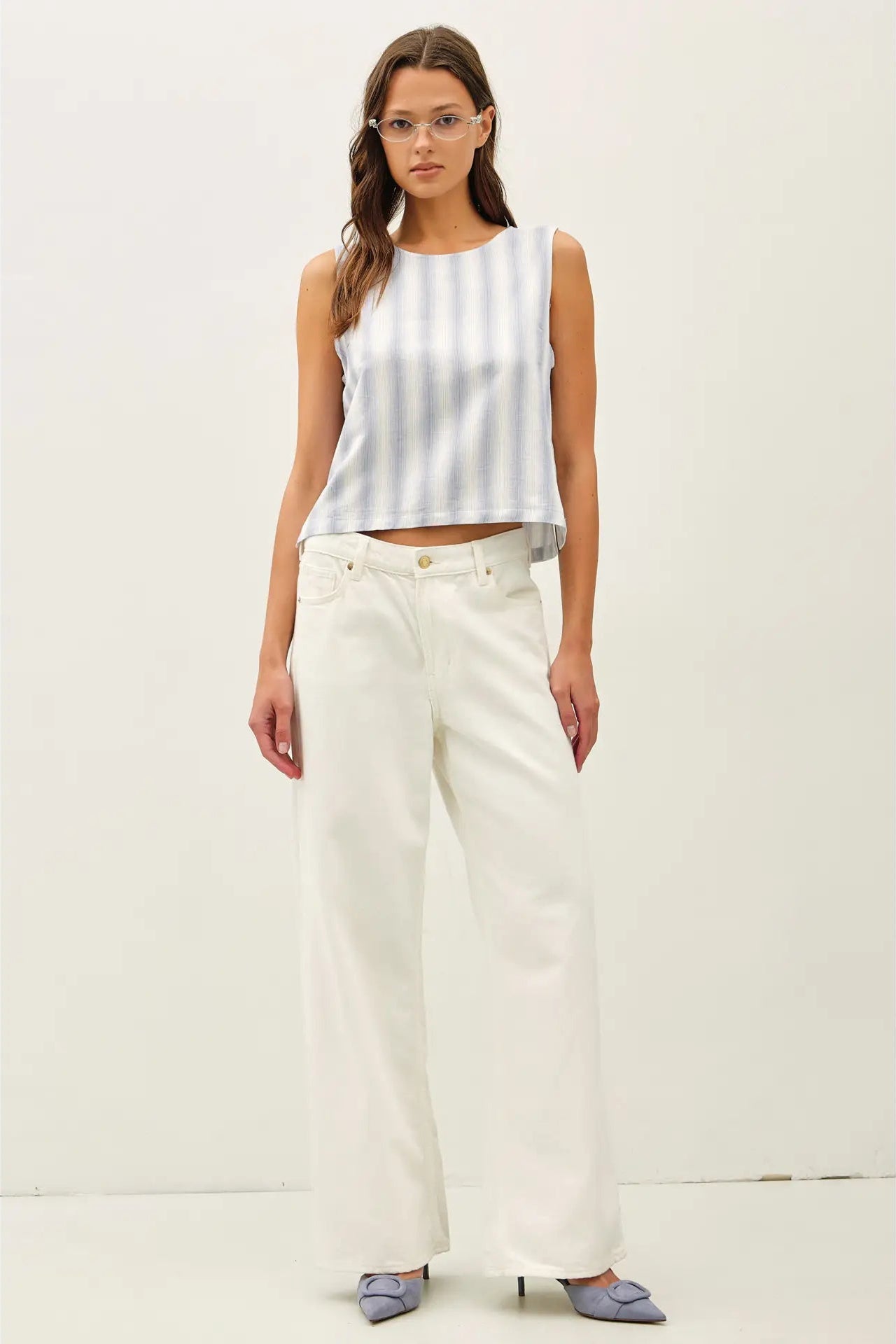 Woman wearing a white sleeveless top and light-colored pants on a plain background