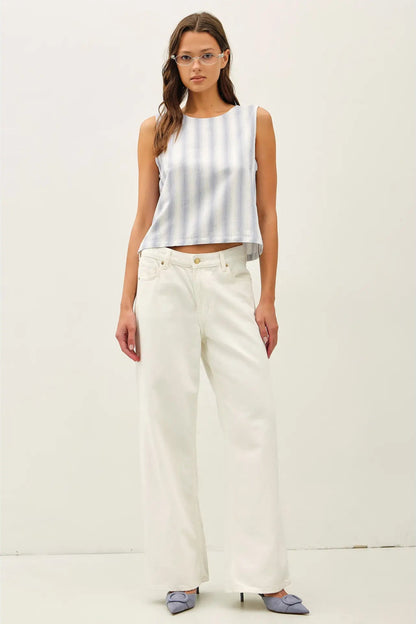 Woman wearing a white sleeveless top and light-colored pants on a plain background