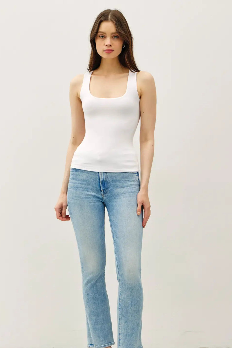 Woman wearing a white tank top and light blue jeans against a plain background