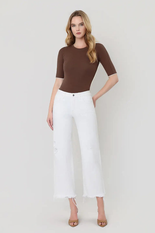 Woman wearing a brown top and white pants on a plain background