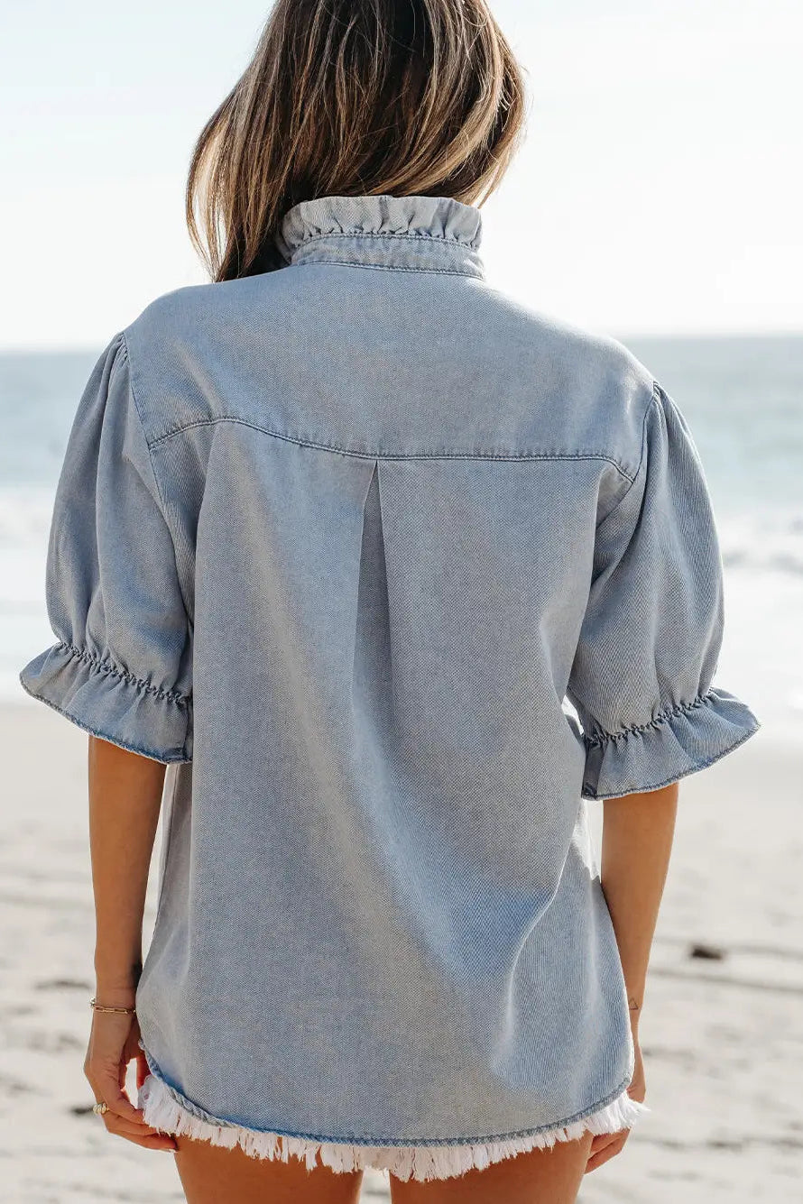 Person wearing a light blue denim shirt on a beach