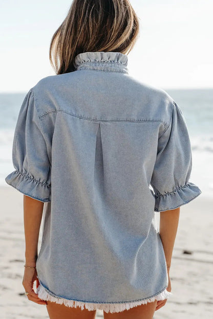 Person wearing a light blue denim shirt on a beach