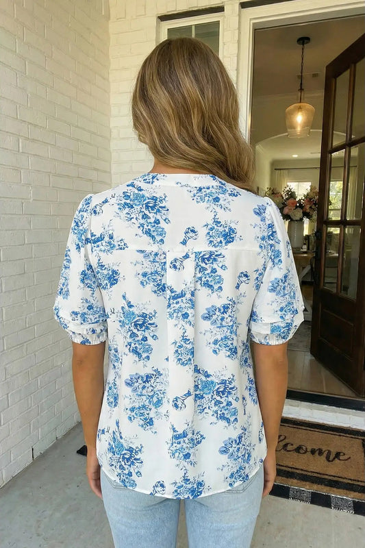 Woman wearing a white blouse with blue floral patterns in a home setting.