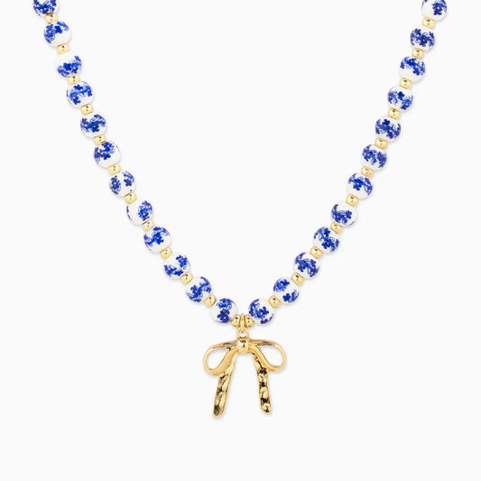 Necklace with blue and gold beads and a gold bow pendant on a white background