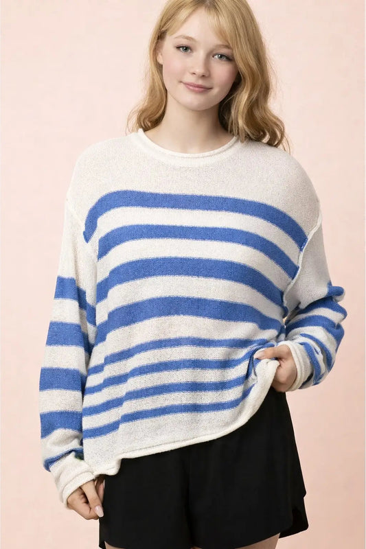 A woman wearing a fuzzy knit sweater with horizontal blue and off-white stripes, paired with black shorts, set against a solid pale pink background.