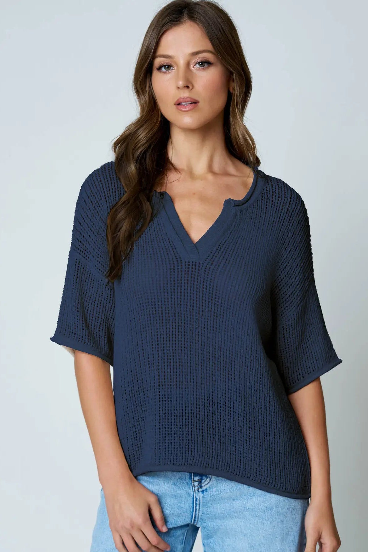 Woman wearing a navy blue knitted top and light blue jeans on a plain background