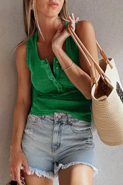 Woman wearing a green top and denim shorts, holding a straw bag against a neutral background