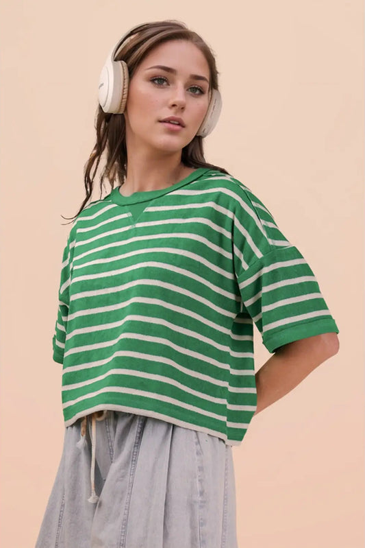 Woman wearing a green and white striped shirt with headphones on a beige background