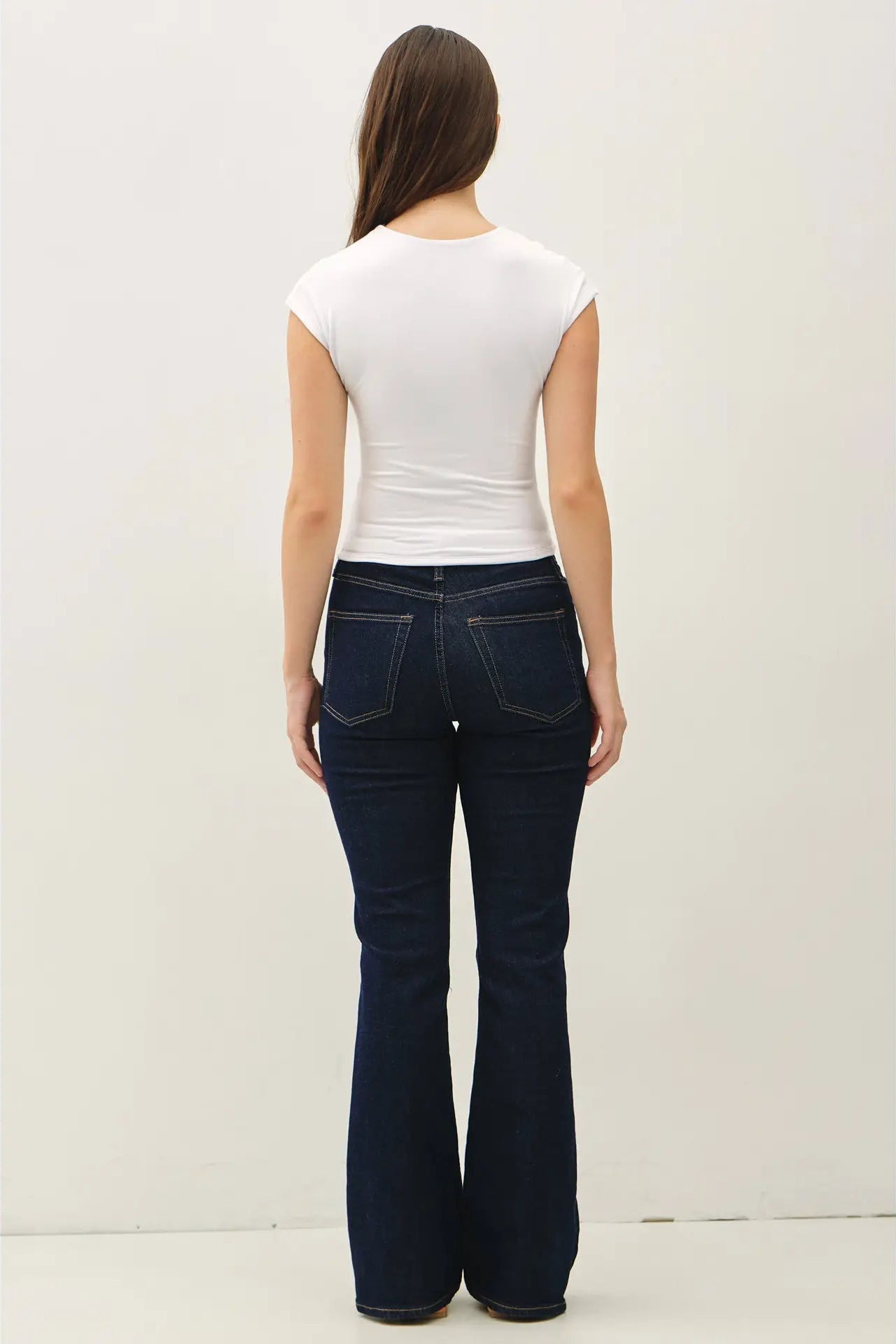 Person wearing dark blue jeans and a white top on a plain background