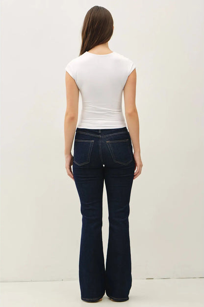 Person wearing dark blue jeans and a white top on a plain background