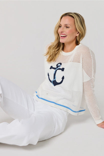 Woman wearing a white sweater with a blue anchor design on a plain background