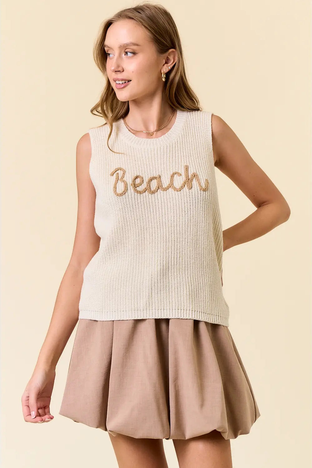 Woman wearing a sleeveless top with 'Beach' text and a skirt on a beige background