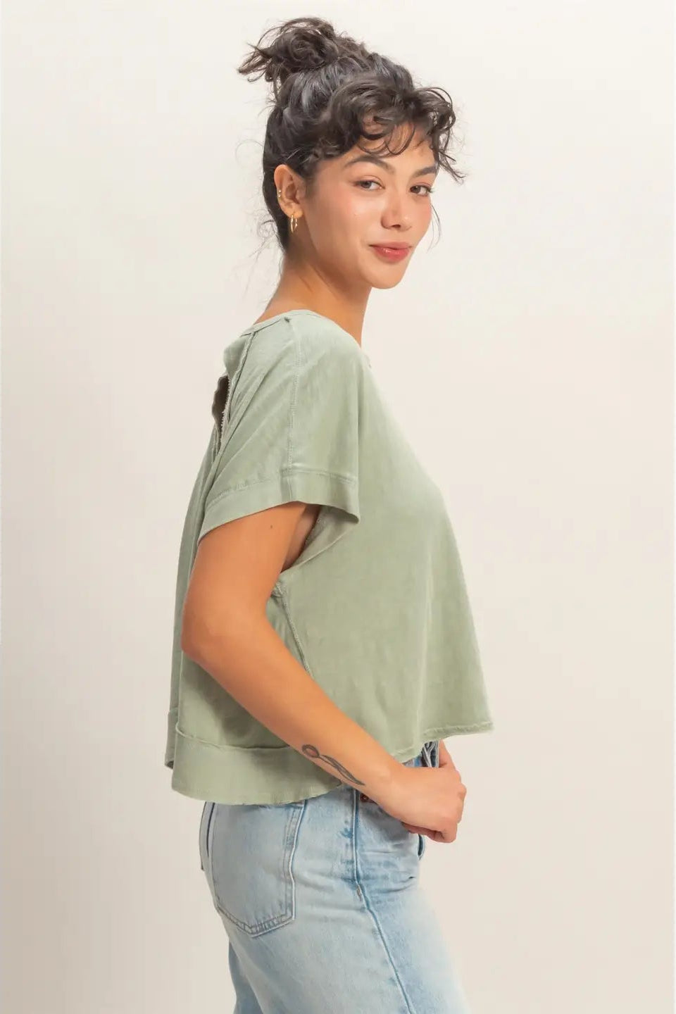 Woman wearing a green t-shirt and blue jeans against a plain background