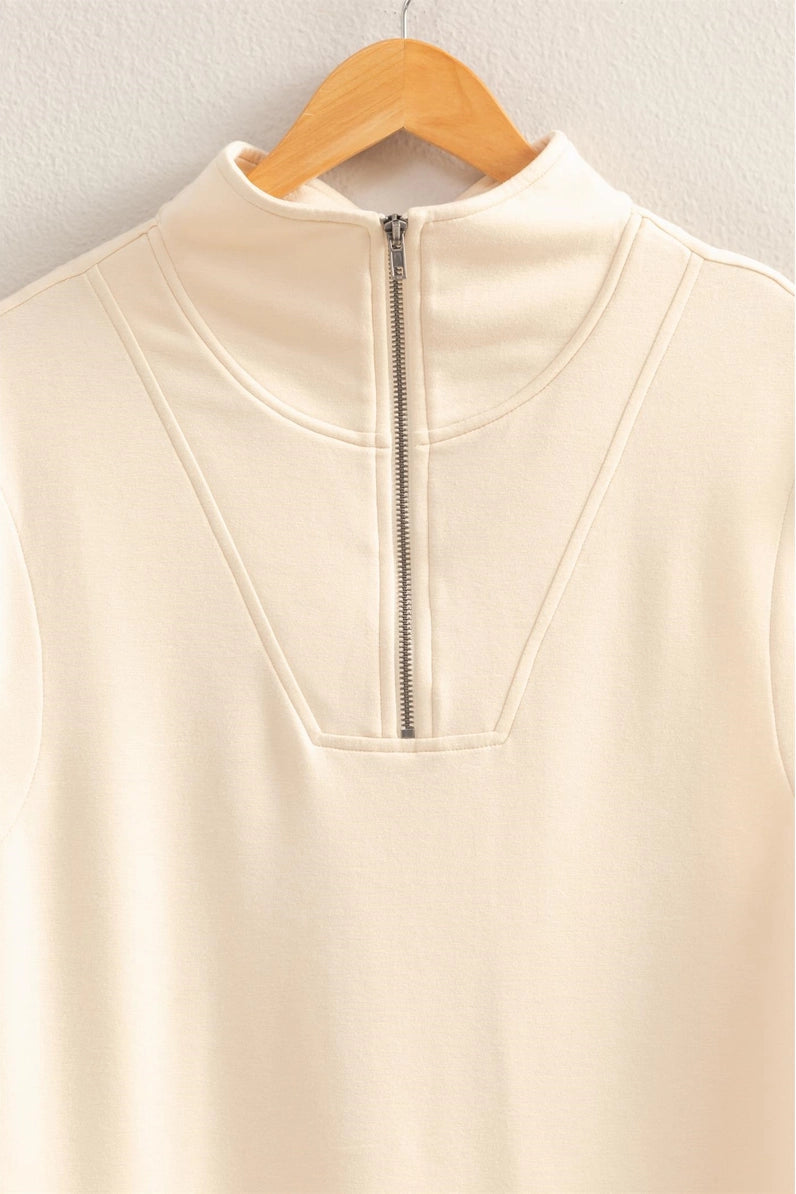 Beige sleeveless top with a zipper on a wooden hanger against a light gray background