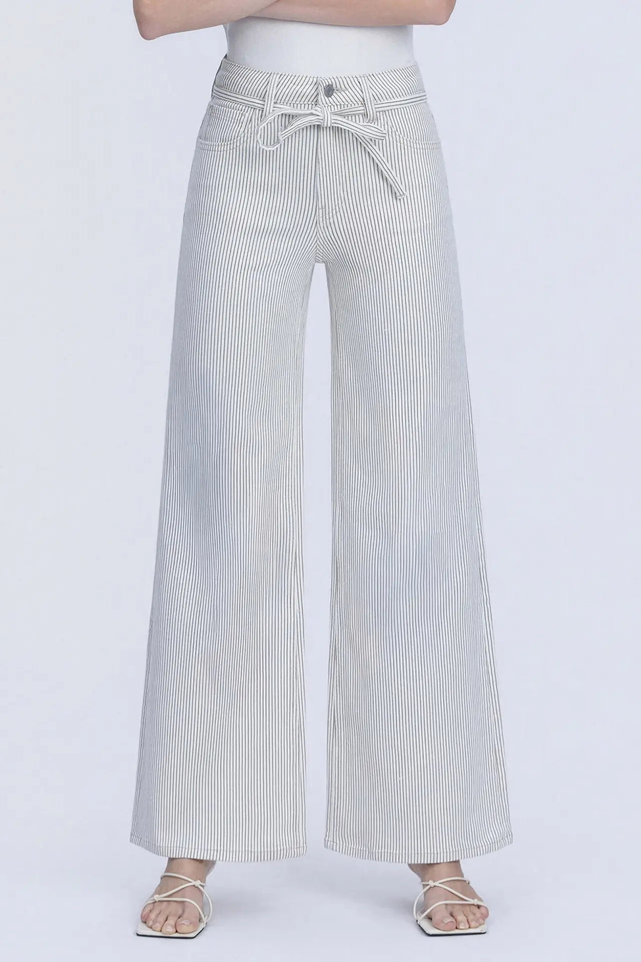 A person wearing light gray wide-leg pants with thin vertical pinstripes and a matching drawstring waist, paired with a white top and clear-strap sandals against a plain light gray studio background.