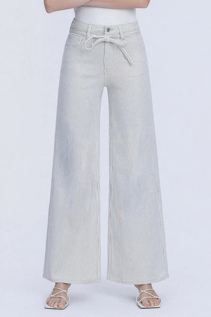 A person wearing light gray wide-leg pants with thin vertical pinstripes and a matching drawstring waist, paired with a white top and clear-strap sandals against a plain light gray studio background.