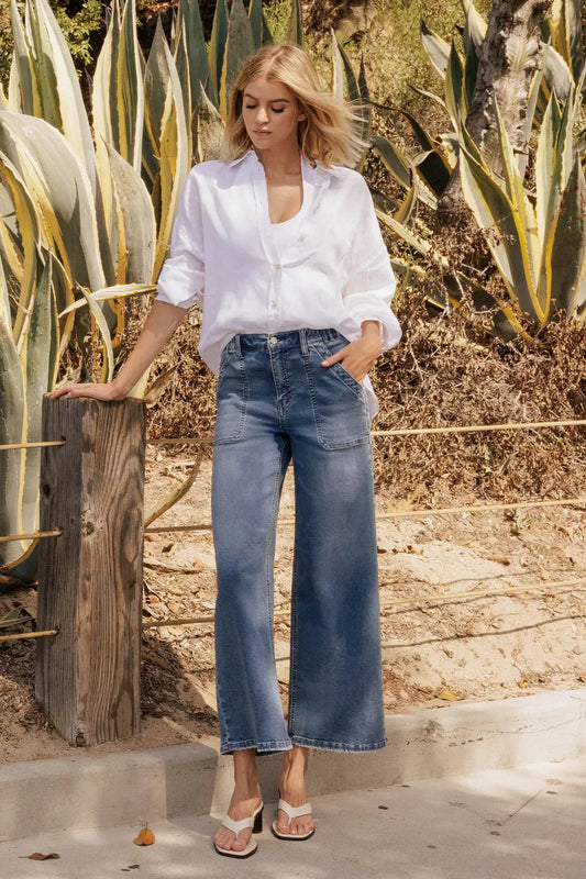 Woman in white shirt and blue jeans standing in a desert-like setting with cacti.