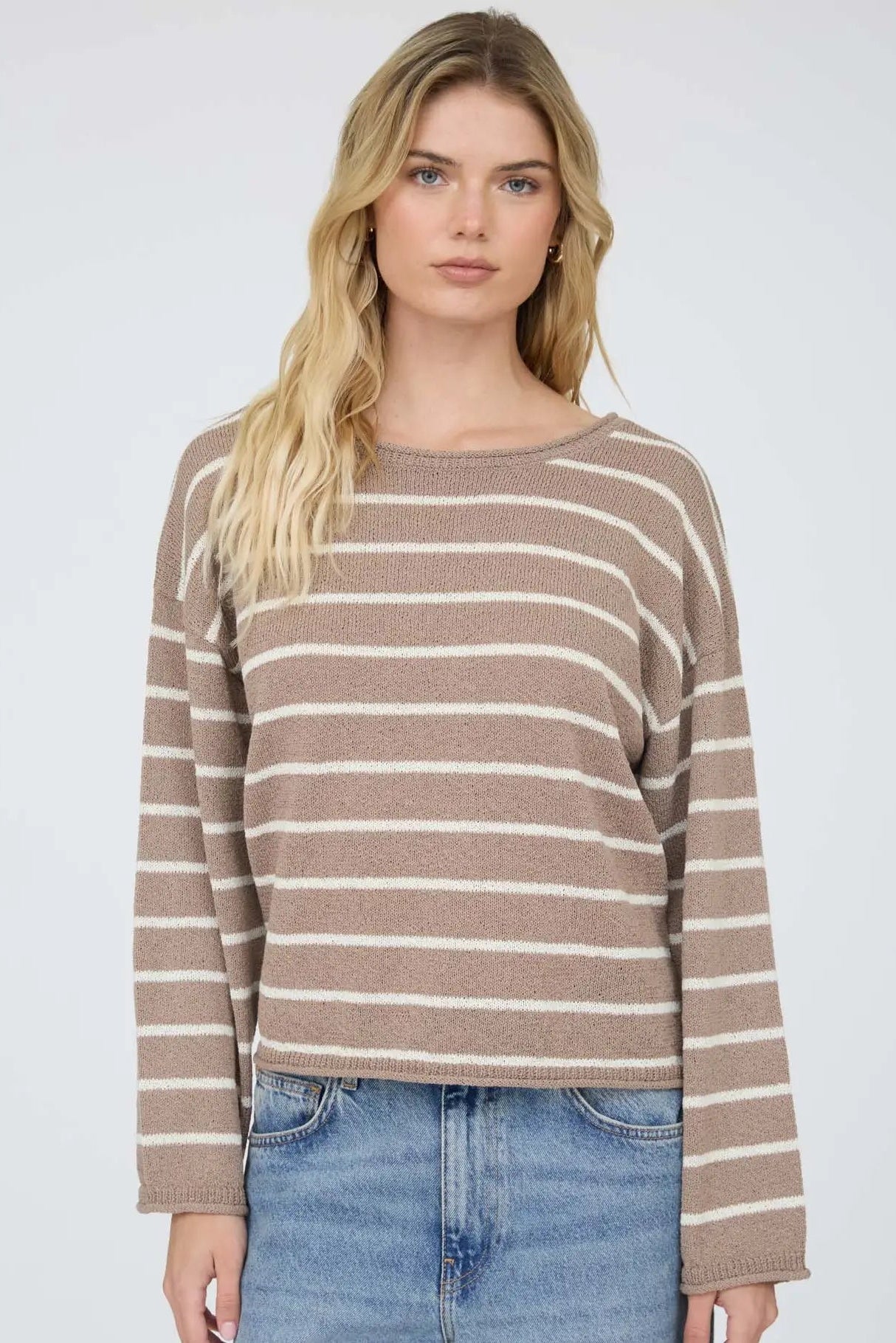 Woman wearing a brown and beige striped sweater with blue jeans on a white background
