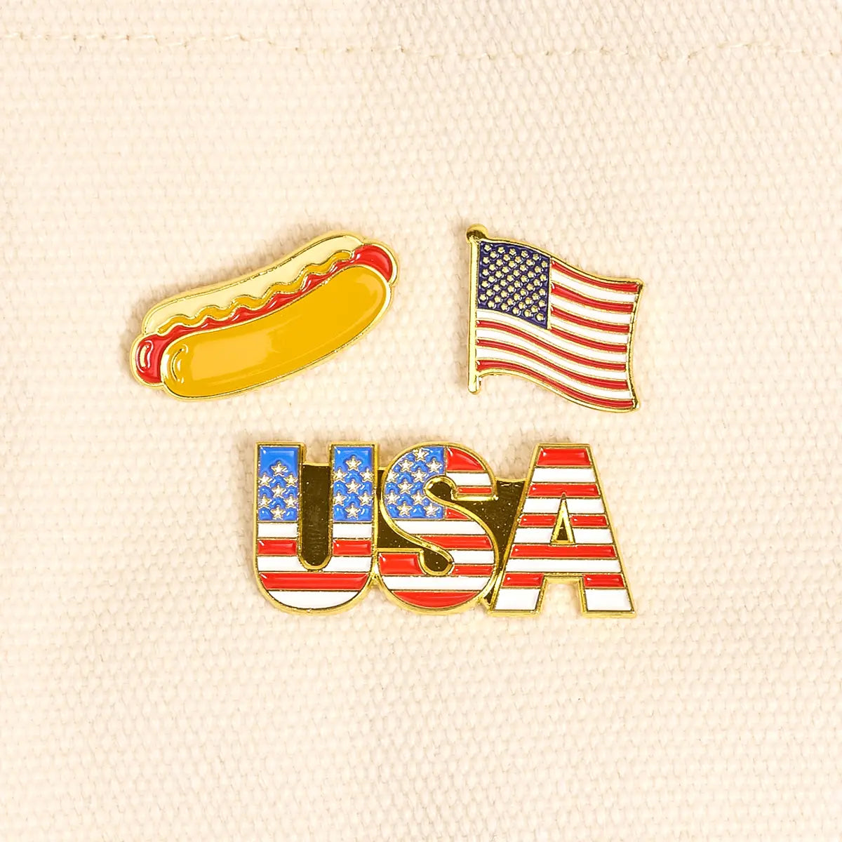 Three pins featuring a hot dog, American flag, and 'USA' text on a textured beige background.