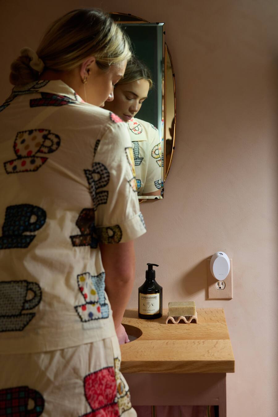 Woman in a patterned robe standing in front of a mirror in a bathroom.