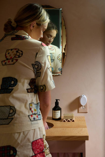Woman in a patterned robe standing in front of a mirror in a bathroom.