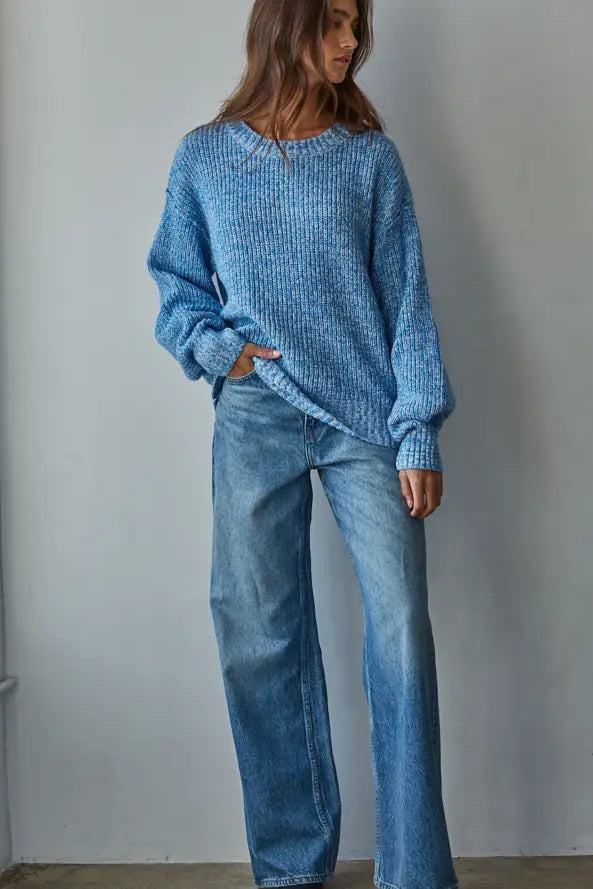 Person wearing a blue sweater and jeans against a plain wall.