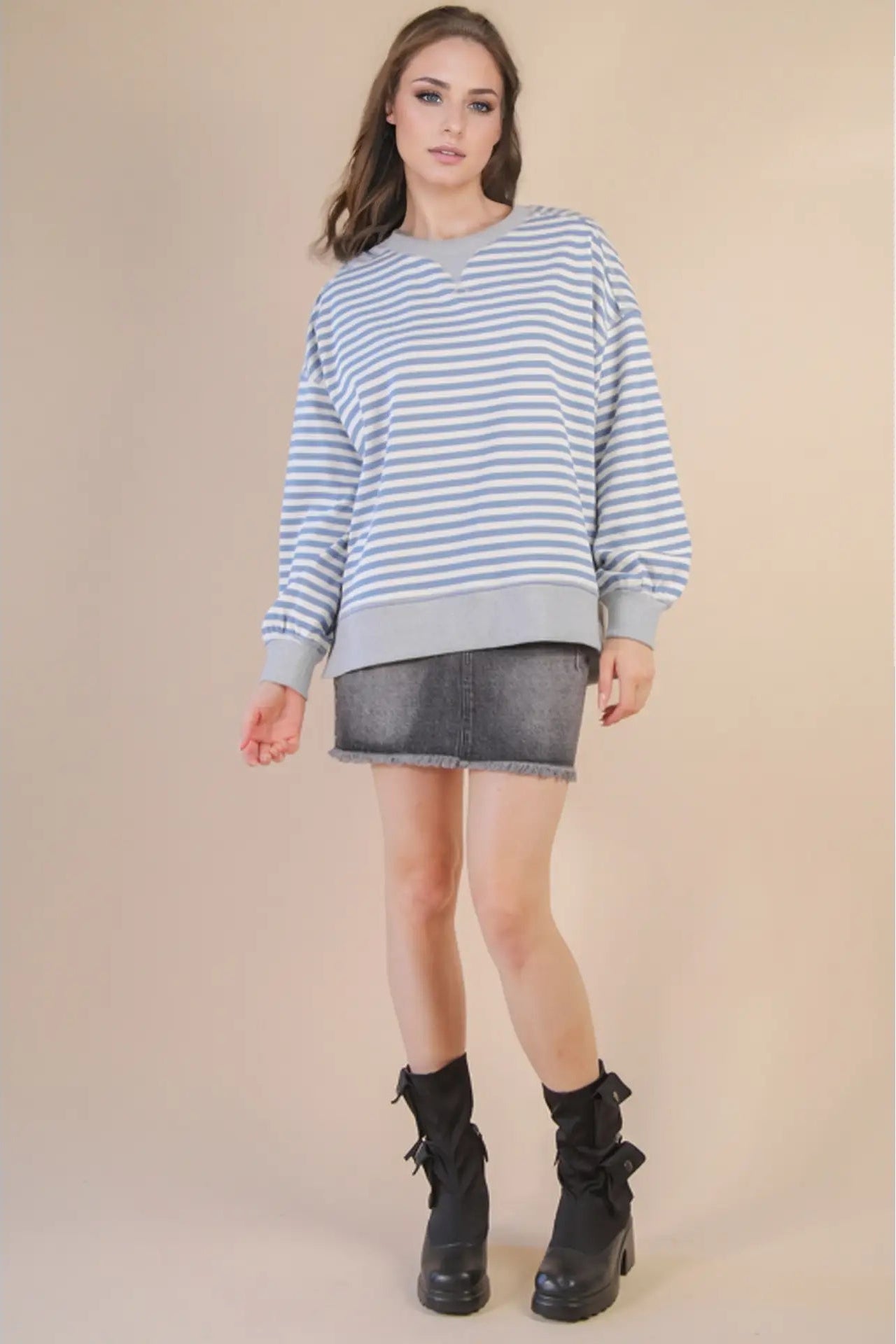 Woman wearing a striped sweater and denim skirt with black boots on a beige background