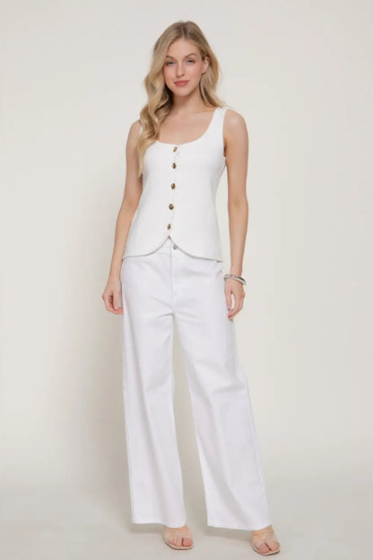 Woman wearing a white sleeveless top and pants on a plain background
