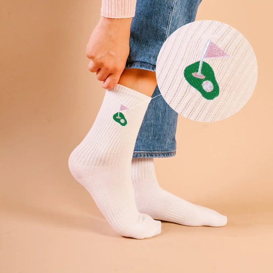 White socks with golf-themed design worn by a person on a beige background