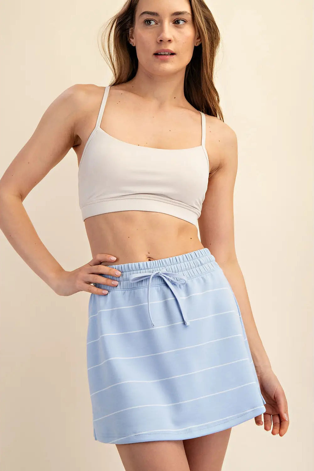 Woman wearing a white crop top and light blue striped skirt on a beige background
