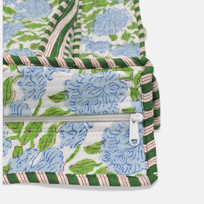Close-up of a quilted fabric accessory with a blue floral print, green and white striped trim, and a white zipper pull on a light gray background.