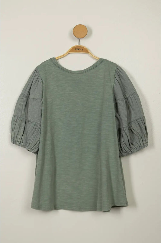 Green dress with puff sleeves on a hanger against a beige background