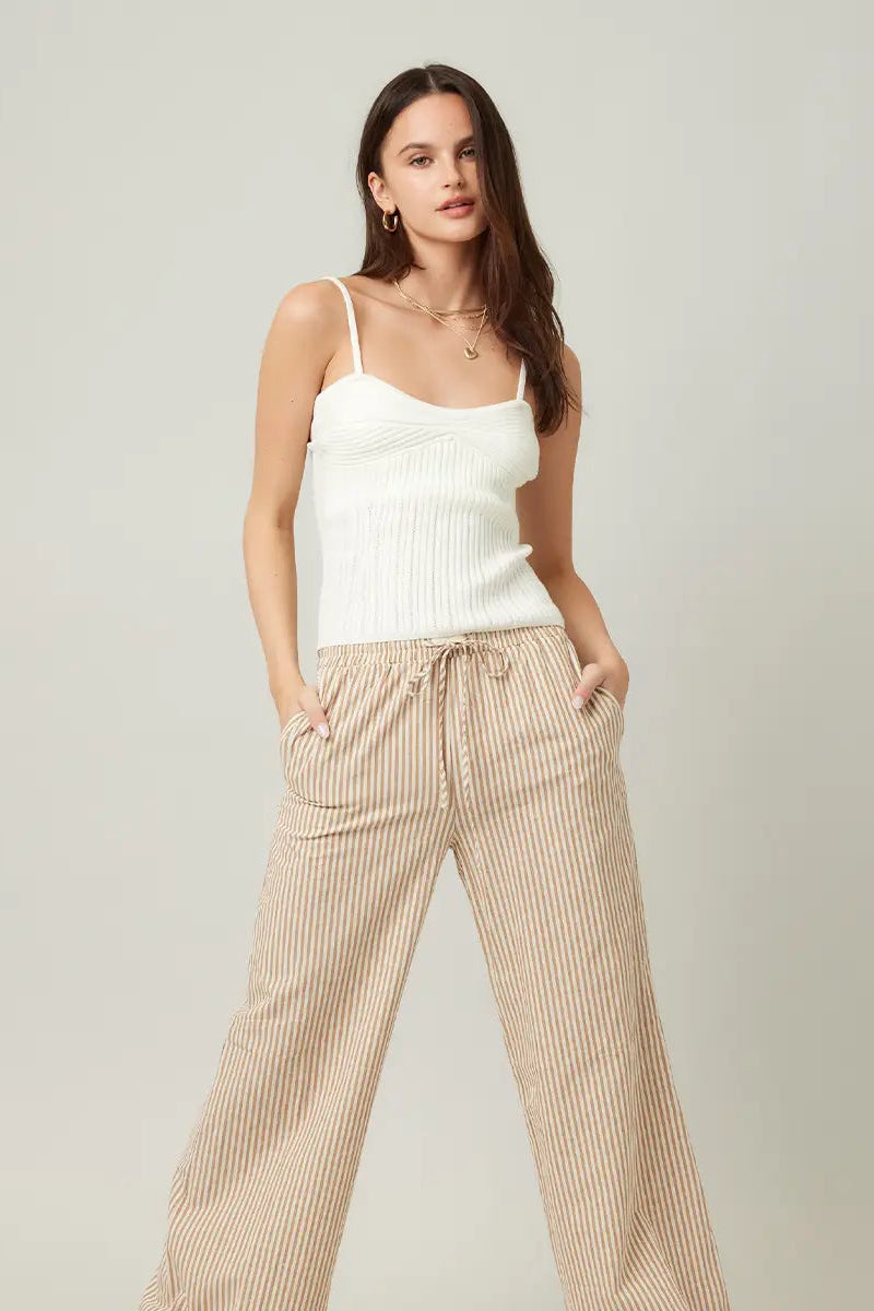Woman wearing a white top and beige striped pants on a plain background