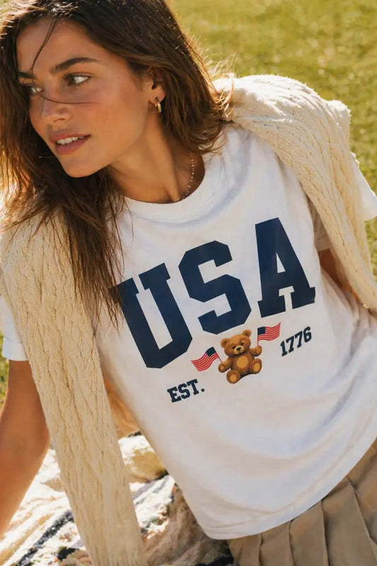 Woman wearing a white t-shirt with 'USA' and teddy bear graphic outdoors.