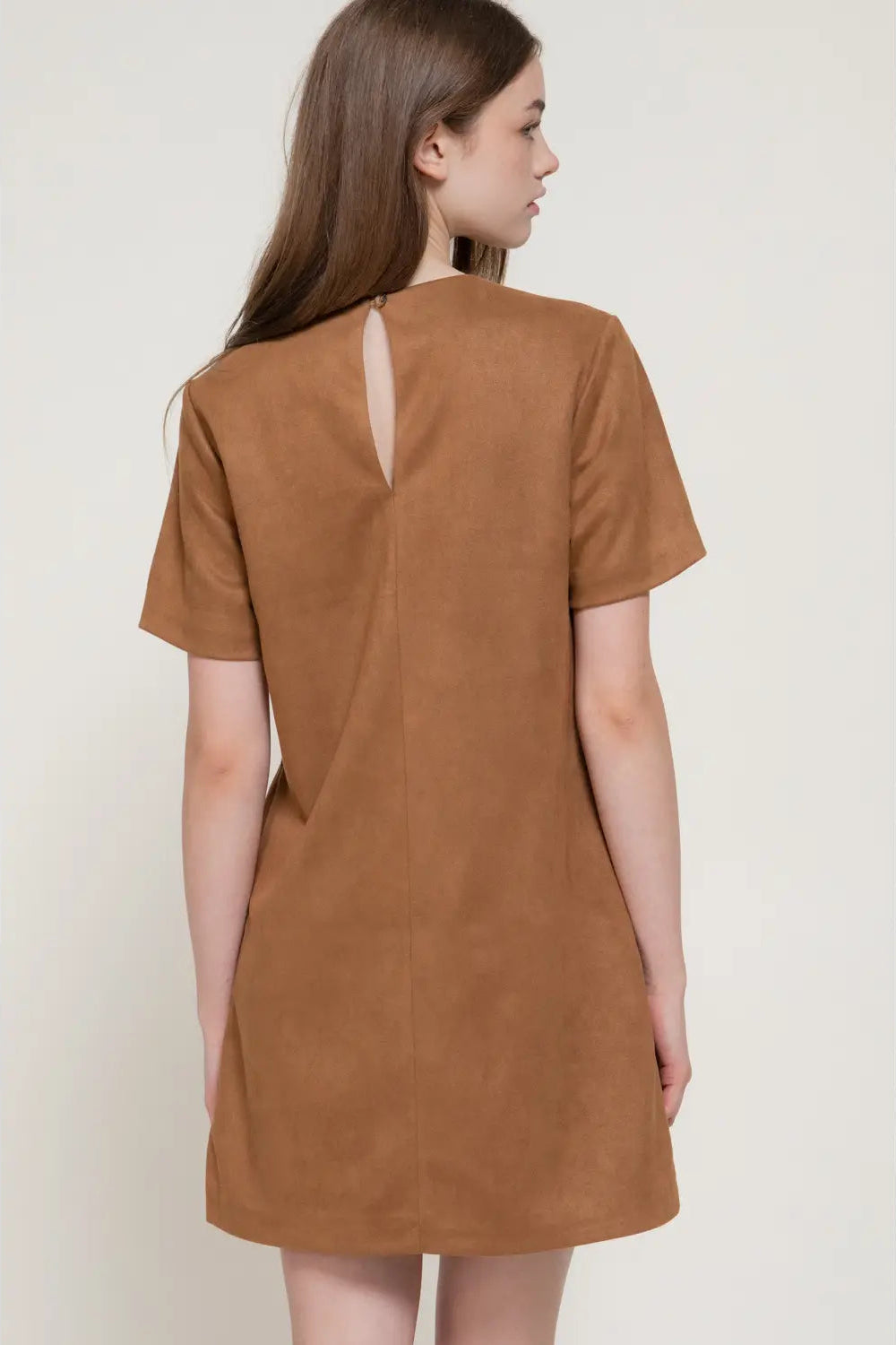 A woman shown from the back wearing a short-sleeve brown dress with a small keyhole cutout at the back, photographed against a plain light beige studio background.