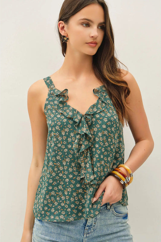 Woman wearing a green floral sleeveless top with ruffles on a plain background