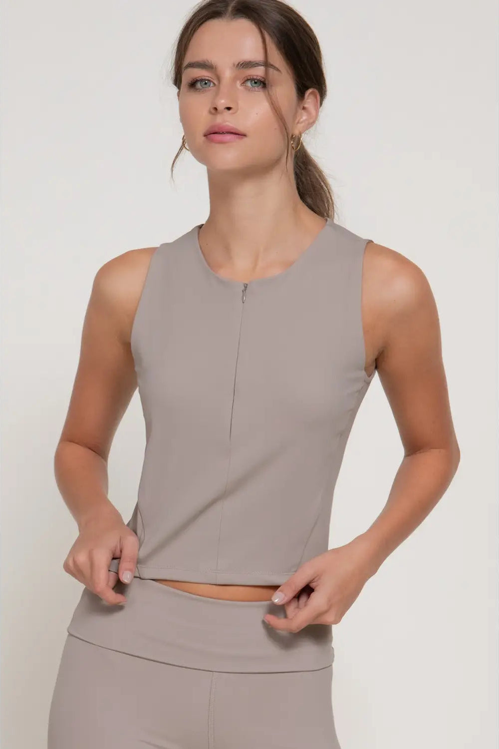 Woman wearing a gray sleeveless top and pants on a white background