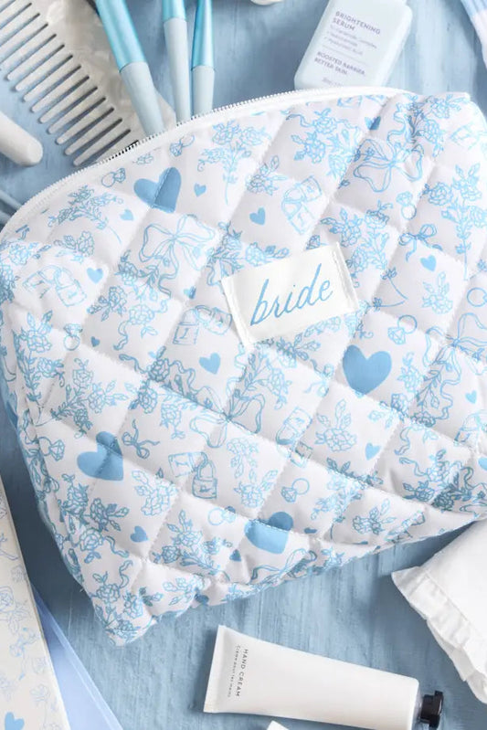 A quilted cosmetic pouch with a white and light blue floral pattern and a central label reading 'bride', styled on a light blue surface with beauty items around it.