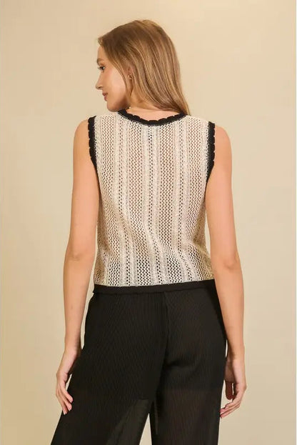 A woman shown from the back wearing a sleeveless knit top with vertical textured stripes in cream and beige, finished with black lace trim at the neckline, paired with black pants, against a solid beige background.