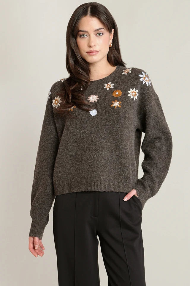 Woman wearing a dark gray sweater with floral patterns on a plain background