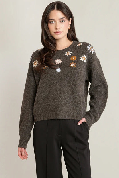 Woman wearing a dark gray sweater with floral patterns on a plain background