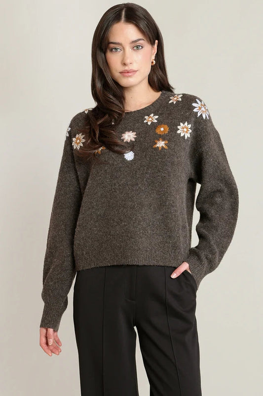 Woman wearing a dark gray sweater with floral patterns on a plain background