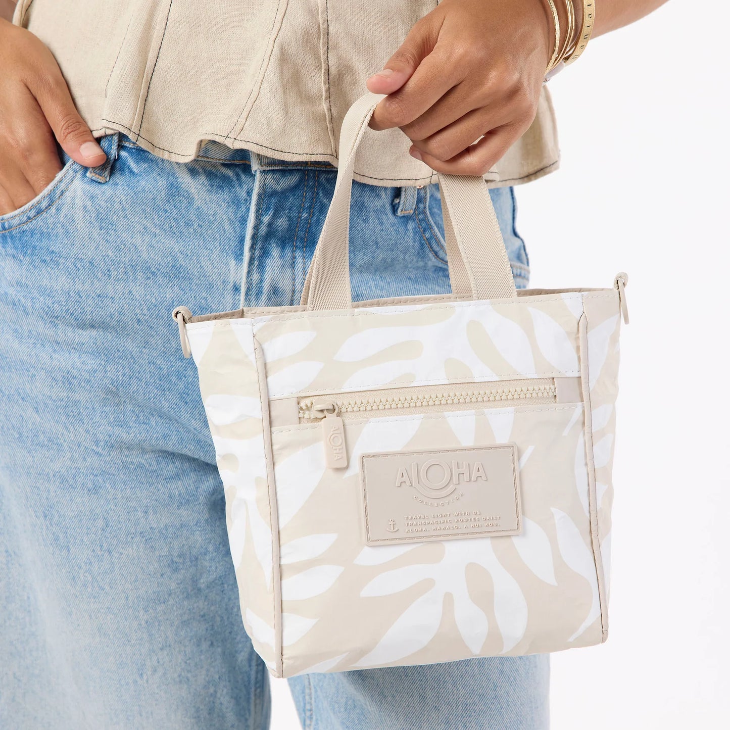 Person holding a beige tote bag with white floral pattern and 'Aloha' label.