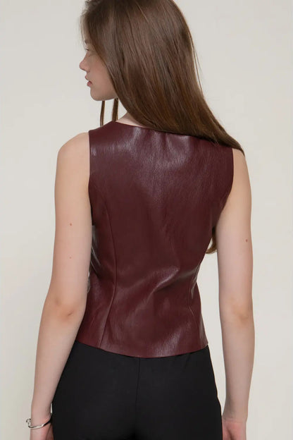 A woman shown from the back wearing a sleeveless, fitted burgundy faux-leather top and black pants against a plain light beige background.