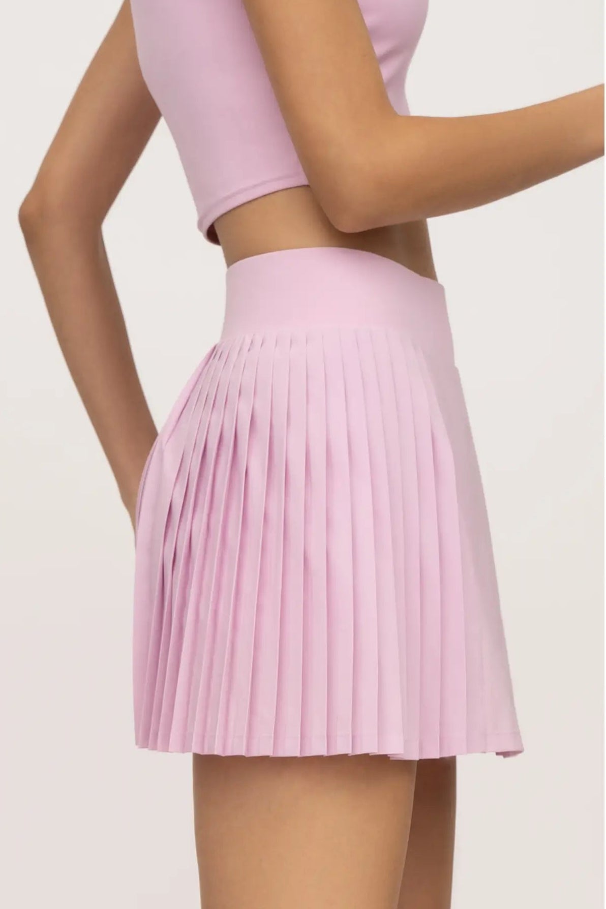 Person wearing a pink pleated skirt on a light gray background
