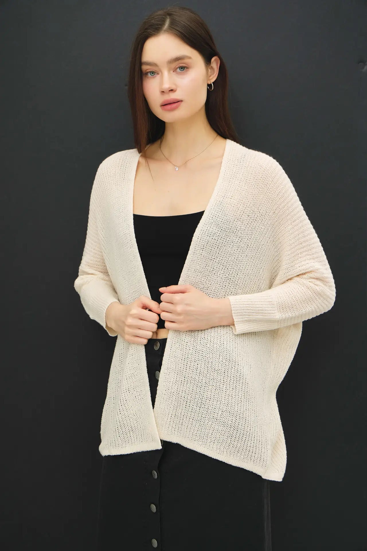 Woman wearing a beige cardigan over a black top against a dark background