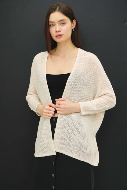 Woman wearing a beige cardigan over a black top against a dark background