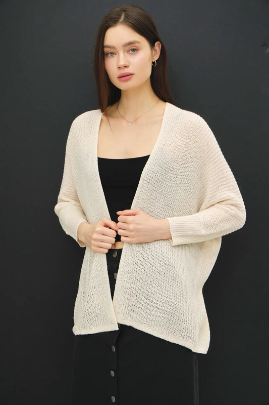 Woman wearing a beige cardigan over a black top against a dark background