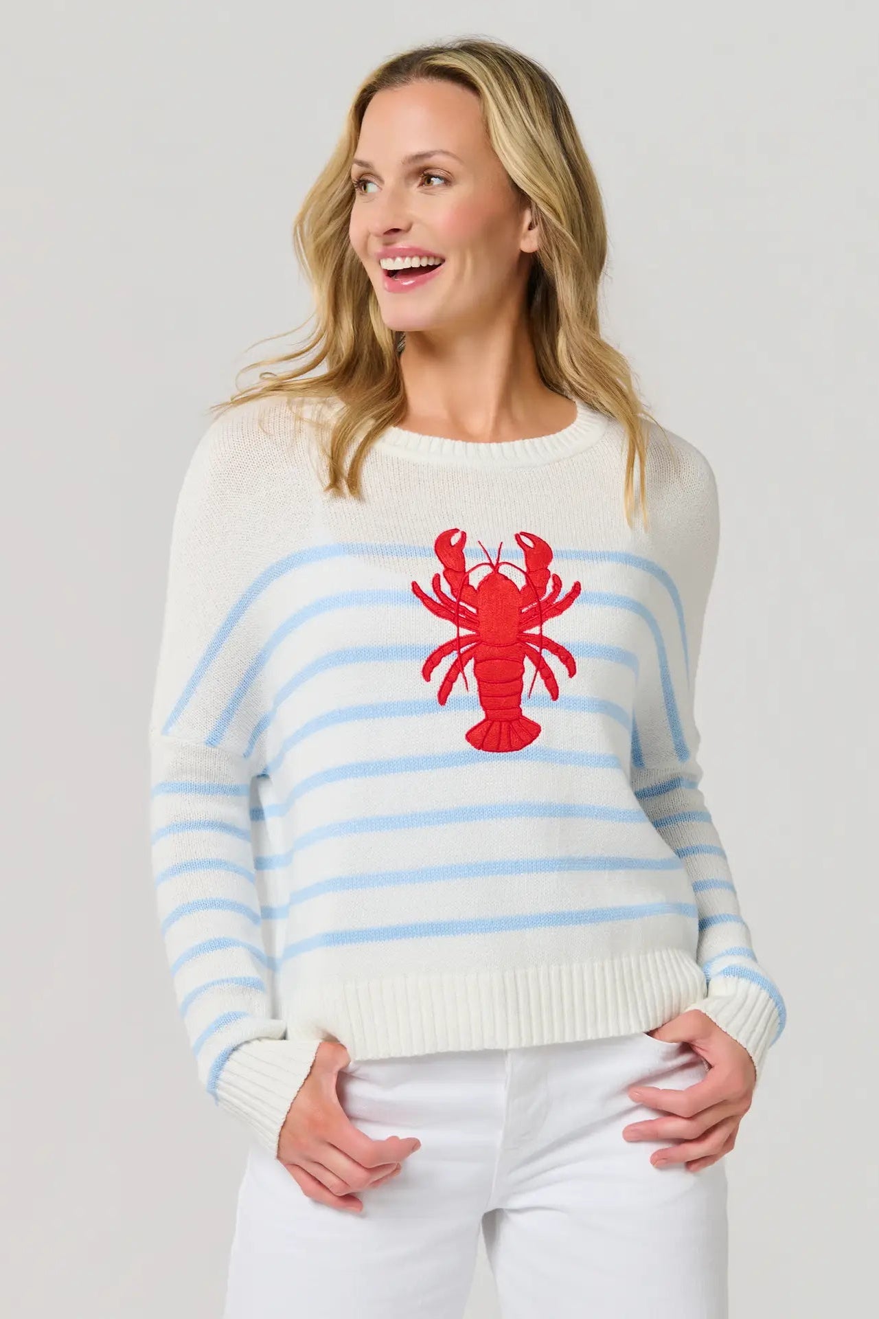 Woman wearing a white sweater with blue stripes and a red lobster design on a plain background