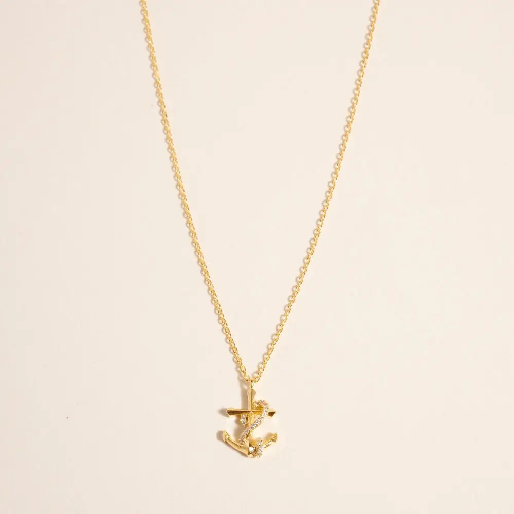 Gold necklace with a small anchor pendant on a beige background